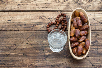 Dried dates fruits on a branch and a glass of water on a wooden table. Traditional fast breaking, Muslims evening meal during holy Ramadan