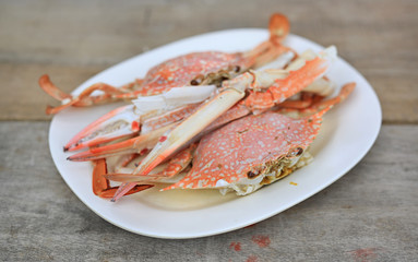 Steamed horse crab or blue crab in white plate on wood table. Seafood in Thailand. Close up.