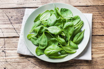 Fresh spinach leaves in bowl on rustic wooden table.