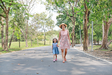 Fototapeta na wymiar Happy Asian mom and daughter walking on street in the summer park.