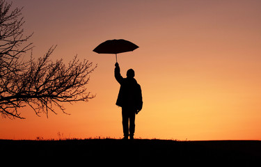 Silhouette boy child with umbrella on sunset background