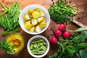A set of products for preparation of healthy salad from new potato, a garden radish, onions, peas and an asparagus with vegetable oil and a basil. The top view, on a wooden surface. Food and health