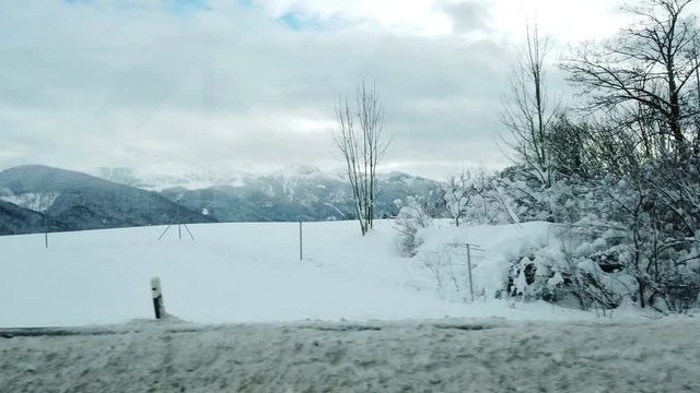 A car is driving on a highway and it is passing trees and a snowy landscape.