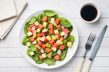 Poke Hawaiian salad with salmon, avocado spinach and vegetables in a plate on a white table.