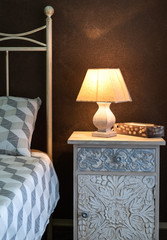Craft bedside lamp on a bedside table in bedroom. Cozy bedroom interior.