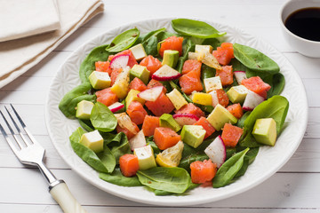 Poke Hawaiian salad with salmon, avocado spinach and vegetables in a plate on a white table.