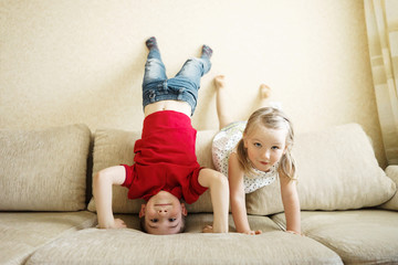 Brother and sister playing on the couch: the boy stands upside down.