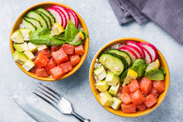 Traditional Hawaiian Poke salad with salmon, avocado rice and vegetables in a bowl on two persons. Top view