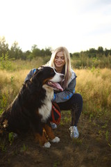 Young woman walking with Bernese Mountain Dog on the summer field