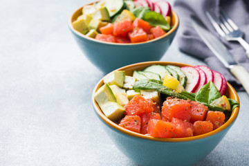 Traditional Hawaiian Poke salad with salmon, avocado rice and vegetables in a bowl on two persons. Copy space