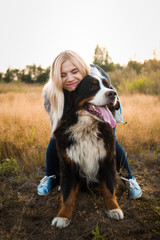 Young woman walking with Bernese Mountain Dog on the summer field