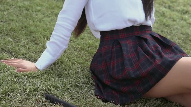 Thai teenager is sitting on grass near katana. Woman inspired by upcoming battle. Girl dreams of good feats and prince. Lady is gorgeous and contented life on green grass. Sword lies on field nearby.