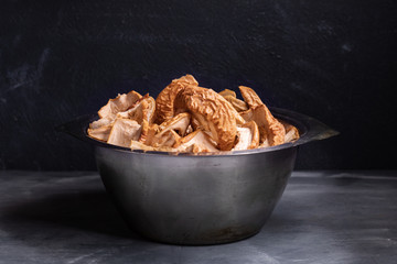 Metal bowl with dried apple slices is standing on dark background.