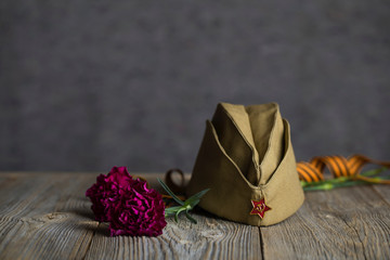 Military cap, carnations, Saint George ribbon on a wooden surface.