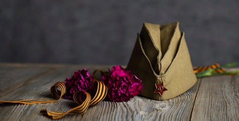 Military cap, carnations, Saint George ribbon on a wooden surface.
