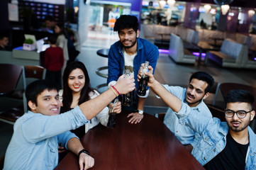 Group of stylish asian friends wear on jeans sitting at table and cheering with soda bottles in club.