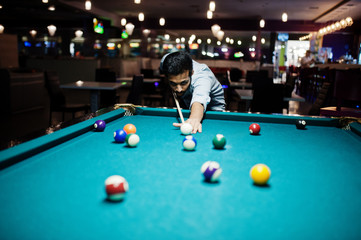 Stylish arabian man wear on jeans playing pool billiard on bar.
