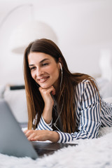 Obraz premium Girl on her laptop at home. Woman using her laptop while lying down. Young female works from home.