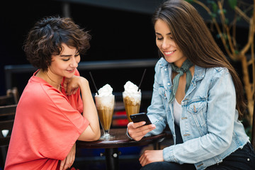 Two girls having a shake at a coffee shop. Girls looking at the phone at a bar.