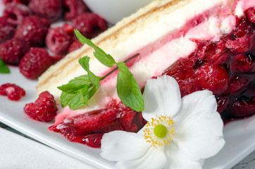 Slice of gourmet fresh raspberry cake on a plate with  fresh summer raspberries  and a white flower in a close up view on a plate 