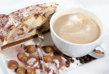 Slice of gourmet fresh hazelnut cholcolate cake on a plate with  fresh hazelnuts and coffee beans in a close up view on a plate with a cup of coffee