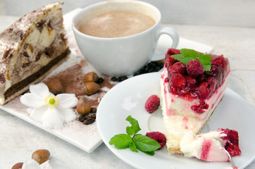 Slice of gourmet fresh raspberry cake on a plate with layered cream topped with fresh summer raspberries in a close up view on a plate with a cup of coffee 