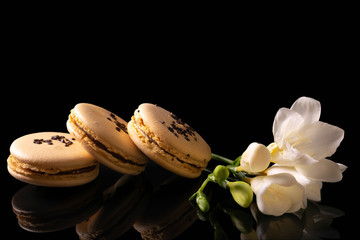 Sweet macarons or macaroons decorated with blooming flowers on a black background.