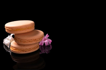 Sweet macarons or macaroons decorated with blooming flowers on a black background.