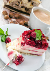 Slice of gourmet fresh raspberry cake on a plate with layered cream topped with fresh summer raspberries in a close up view on a plate with a cup of coffee 