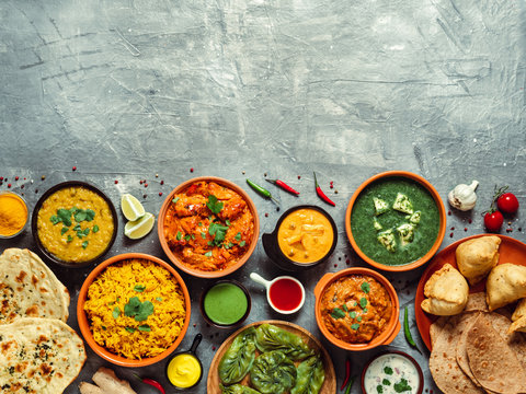 Indian cuisine dishes: tikka masala, dal, paneer, samosa, chapati, chutney, spices. Indian food on gray background. Assortment indian meal with copy space for text. Top view or flat lay.