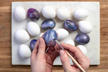 Female hands hold an egg and a tassel and make a cosmic pattern on the background of eggs on marble