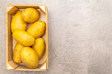Raw unpeeled young potatoes in a wooden crate. New harvest, on stone background, copy space, top view