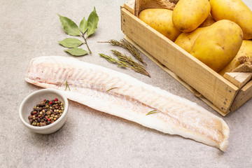 Raw young potatoes and frozen hake fillets. Ingredients for fish and chips. Spices and herbs on a stone background, close up.