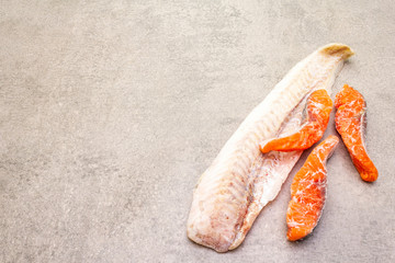 Assorted frozen fish. Hake fillet and salmon pieces. Ingredients for healthy food cooking. Stone culinary background, copy space.