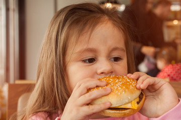 Little child eating a hamburger in the cafe