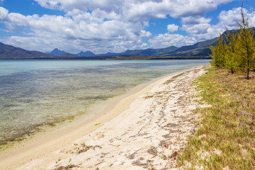 Wild beach with white sand and transparent sea surrounded with mountains and lush tropical plants, Mauritius island