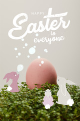pink painted chicken egg on green grass with happy Easter to everyone lettering and rabbits illustration