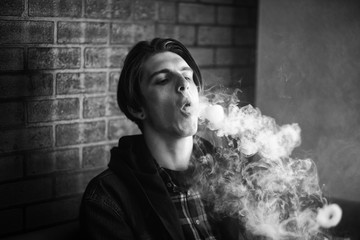 Vape teenager. Portrait of young handsome guy smoking an electronic cigarette in the bar. Bad habit that is harmful to health. Vaping activity. Black nad white.