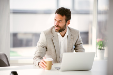 Obraz premium Manager drinking coffee while working on laptop. Businessman sips coffee while he works.