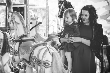 A stylish mother in a red dress and a black jacket and a little daughter in a leather jacket for a walk in the city in an amusement park. The family is having fun and experiencing life