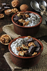 Two cups with yogurt with chia seeds, walnuts and dark chocolate. Breakfast or dessert for two. Healthy food. Keto diet. Diet recipes ideas. Shabby style. Dark background.