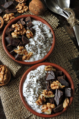 Two cups with yogurt with chia seeds, walnuts and dark chocolate. Breakfast or dessert for two. Healthy food. Keto diet. Diet recipes ideas. Shabby style. Dark background.