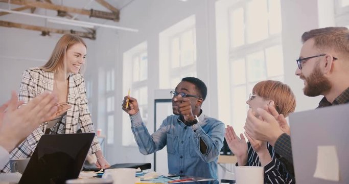 Young millennial African American office employee speaking at multiethnic workplace team meeting, everyone clapping him.