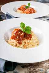 Close-Up meatballs in tomato sauce with spaghetti on white plates, cherry tomatoes on a wooden table.