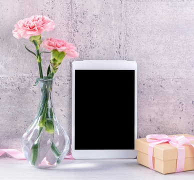 Home decor with blooming carnation and tablet as photo frame beside wall on the table - Close up, copy space, mock up, beautiful mothers day concept.