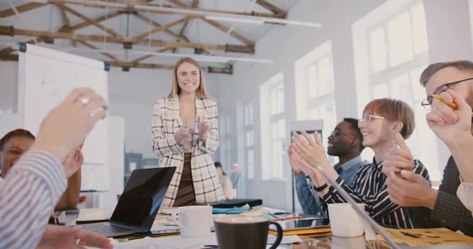 Young millennial businessman speaking at creative multiethnic modern office team meeting, everyone clapping and smiling.