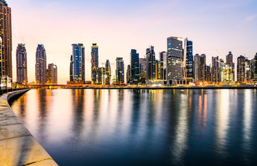 Obraz na płótnie Canvas Stunning view of the illuminated Dubai skyline during sunset buildings and skyscrapers reflected on a silky smooth water flowing in the foreground. Dubai.