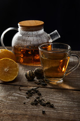 transparent teapot with blooming tea, cup, lemons and tea balls on wooden table isolated on black
