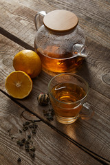 transparent teapot with cup of traditional chinese blooming tea and lemons on wooden surface