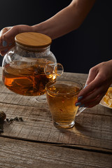 cropped view of young woman pouring blooming tea from teapot in cup isolated on black
